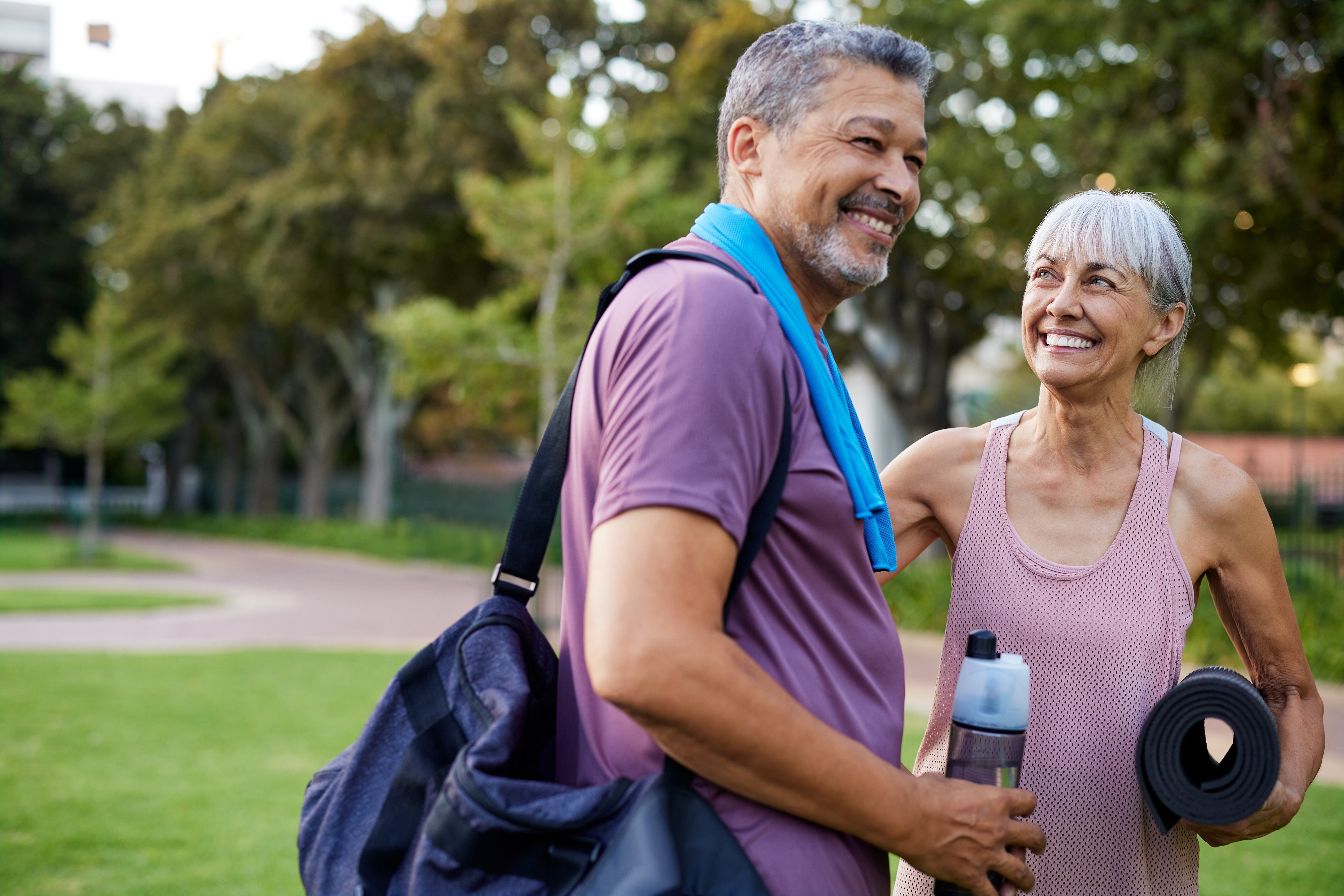 An active, smiling older couple with workout gear in a sunny park